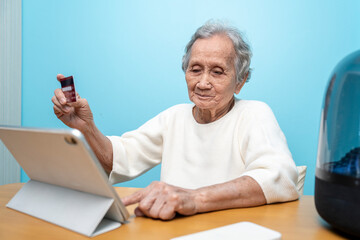 An elderly Asian woman holds a credit card to pay for goods via tablet, online shopping, contactless payment