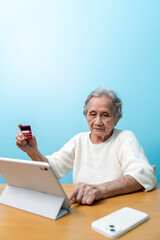 An elderly Asian woman holds a credit card to pay for goods via tablet, online shopping, contactless payment