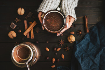 Top view of female hands in sweater holding mug of hot chocolate drink on rustic wooden background,...