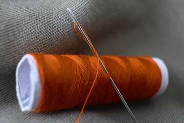 Bright orange thread and needle on fabric surface