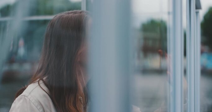 Beautiful young woman inside glass cabin waving hand on glass and smiling, panning shot
