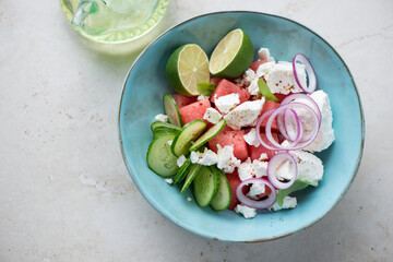 Turquoise bowl with watermelon and feta cheese salad, horizontal shot on a light-beige stone background, high angle view