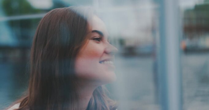 Beautiful young woman inside glass cabin making funny face at window, smiling and placing hand on glass
