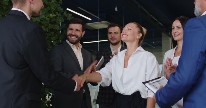 Handshake of happy leader and manager, smiling colleagues greeting new employee with applause in modern office. Woman and man shake hands, business team clapping for hiring celebration on meeting