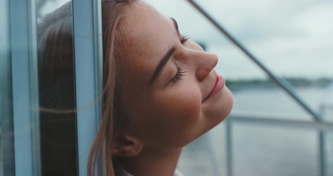 Cose-up of a beautiful young woman resting head on glass cabin wall closing eyes and opening them to look up

