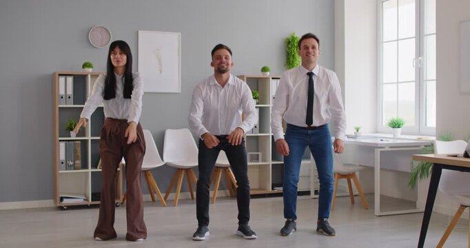 Three coworkers do office squats, taking a brief exercise break to boost energy. Coordinated movement promotes fitness, posture and teamwork. Quick routine boosts team energy at workplace.