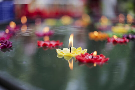 Colorful floating flower candle light with bright flame illuminates water surface. Yellow, red, pink, and orange blossoms float peacefully in evening, creating serene and spiritual atmosphere