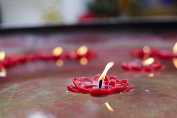 Red lotus shaped candle floating water, emitting warm glow. Spiritual ambiance fills scene, evoking...