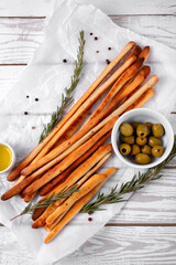 Grissini made of wheat flour with parmesan, rosemary and olive oil. Breadsticks served with olives on white background. Italian crispy snack. Top view