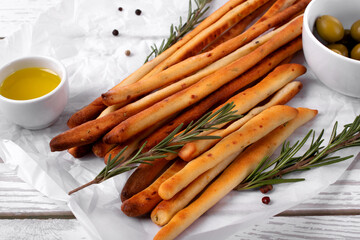 Grissini made of wheat flour with parmesan, rosemary and olive oil. Breadsticks served with olives on white background. Italian crispy snack