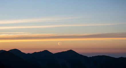Fototapeta premium Stunning Twilight Sky Gradient with Crescent Moon Over Dark Mountains A mesmerizing natural landscape captured during the tranquil moments of sunset or sunrise