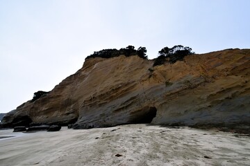 A coastal cliff on Tanegashima Island, Japan, showing visible layers of sedimentary rock strata and a sea cave on a sandy beach.
