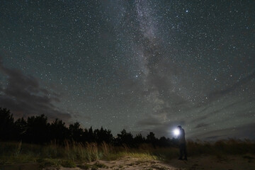 A lone adventurer holding a bright flashlight stands in awe under the breathtaking Milky Way galaxy on a clear night.