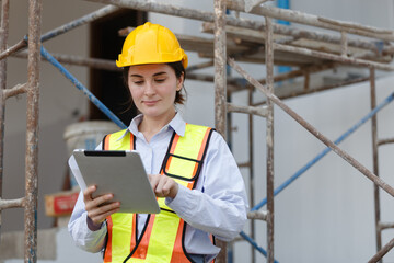 Female engineer in safety vest and helmet using tablet for construction site assessment, representing modern project planning, data management, and digital transformation in civil engineering.