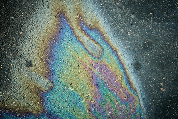Oil, gasoline, or fuel spill on asphalt pavement displaying iridescent rainbow colors.