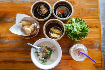 Traditional Thai Breakfast. Dim sum, congee, fried dough sticks, Thai tea on wooden table. A peaceful early morning in Thailand. High angle view of breakfast on table.