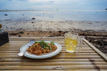 A glass of beer and Pad Thai a dish of dried thin rice noodles stir fried with tamarind sauce mixed In eggs and chopped firm tofu, Thai food. Thai famous street food, traditional Pad Thai.