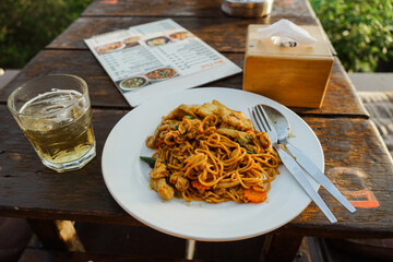 A Glass of Beer and Stir fry rice noodles with vegetables and meat on Wooden Table.