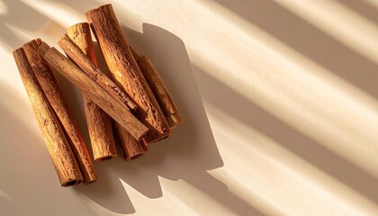 Pile of cinnamon sticks casting warm shadows on a light surface.

