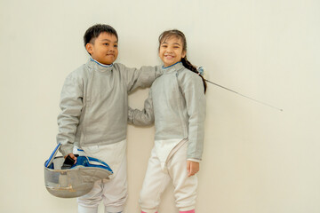 Side view of Asian brother and sister with fencing sport uniform hug together also look at face and smile to relax during practice for competition.