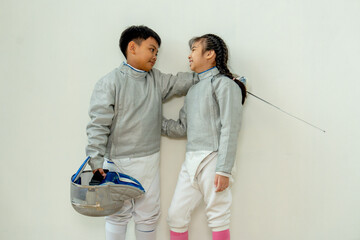 Asian brother and sister with fencing sport uniform hug together also look at face and smile to relax during practice for competition.