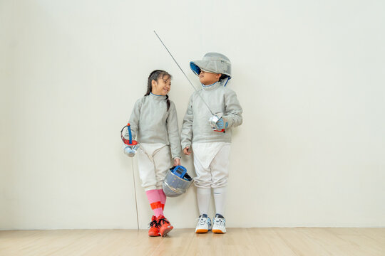 ฺAsian brother and sister with fencing sport uniform stand beside  also look at face and smile to relax during practice for competition.