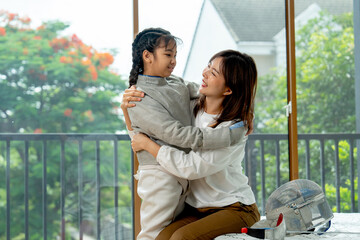 Close up Asian mother sit on bed and hug together with her daughter during practice fencing sport in bedroom with soft morning light and happiness.
