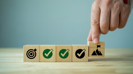 A close-up photograph of wooden blocks with business-related icons arranged in a row on a light wooden surface