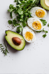 Close-up of halved boiled eggs, sliced avocado, and fresh herbs on a white background with copy space.