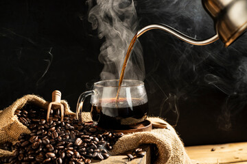 Pour hot coffee into a coffee cup With roasted coffee beans arranged on a table on a black and dark background.