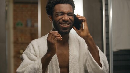 African American man in bathroom talking mobile phone guy after shower morning shaving beard...