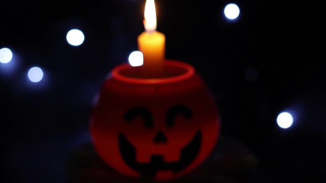 Un primer plano de una calabaza de halloween desenfocada y con una vela con fuego dentro, con un fondo negro con luces desenfocadas. Feliz halloween