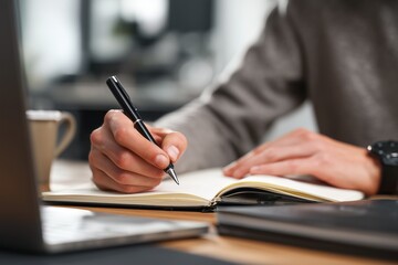 Professional Businessperson Handwriting in Notebook at Desk with Laptop and Coffee Mug
