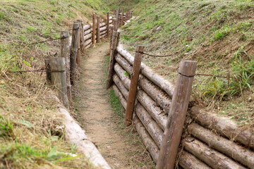 Empty military trench, reinforced with timber and wire, surrounded by grass