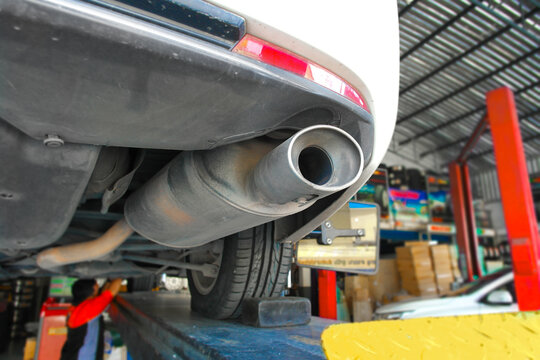 Car exhaust pipe and muffler close up under vehicle on lift, concept of automotive emission system, exhaust inspection, muffler maintenance and repair service in auto garage workshop