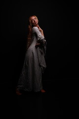 Full length portrait of a young red-haired woman in a vintage white dress in a low key