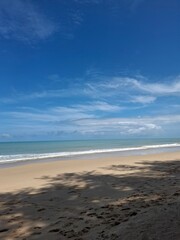 Fototapeta premium Wide view of sandy shoreline with ocean waves under a blue sky with scattered clouds du daytime, showing a peaceful coastal landscape and beach scene