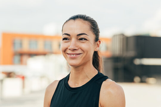 Portrait of a young cheerful female athlete standing on the roof - Powered by Adobe