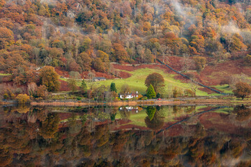 Lake district autumn landscape with house by water reflecting foliage