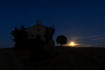 Chapel and tree silhouette during a dramatic moonrise creating atmospheric night scene