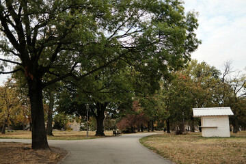 Pathway lined with trees and small white kiosk in Kalemegdan Park during autumn in Belgrade.