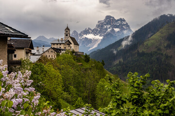 Church perched on steep sided hill in Colle Santa Lucia village with dramatic Dolomites peak of Monte Pelmo rising from forested valleys