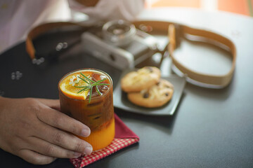 A refreshing iced coffee with orange juice garnish, decorated with rosemary and a small flower