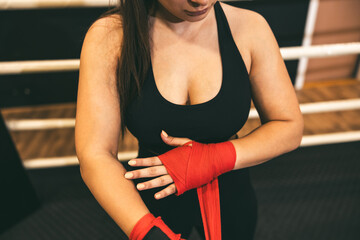 Female boxer wraps hands in red tape before training in a gym