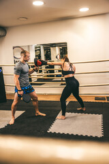 Dynamic training session in a boxing gym with a female fighter and her coach focusing on technique and strength
