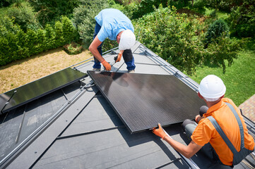 Workers building photovoltaic solar panel system on rooftop of house. Men technicians in helmets and gloves installing solar module with help of hex key outdoors. Alternative energy generation concept