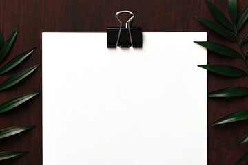 White paper held by clip with green leaves on dark wood
