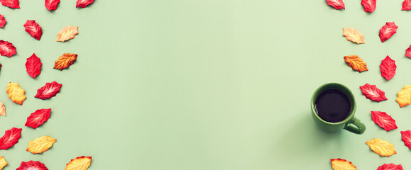 A cup of coffee and autumn leaves on a green pastel background