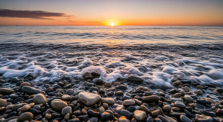 Obraz premium Tranquil coastal waters at twilight, with the sun descending over the vast ocean, illuminating the wet, smooth pebbles on the peaceful shore as gentle waves break softly