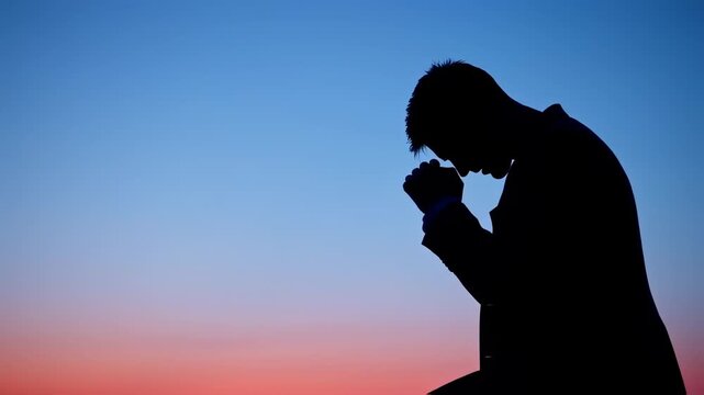 Silhouette of a man praying at sunset with colorful sky.